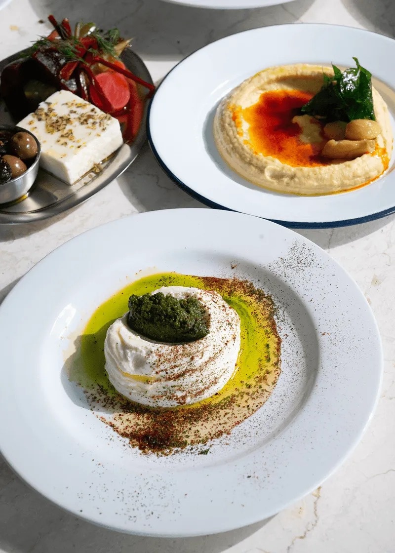 Whipped feta, hummus and other spreads on white plates at Estia