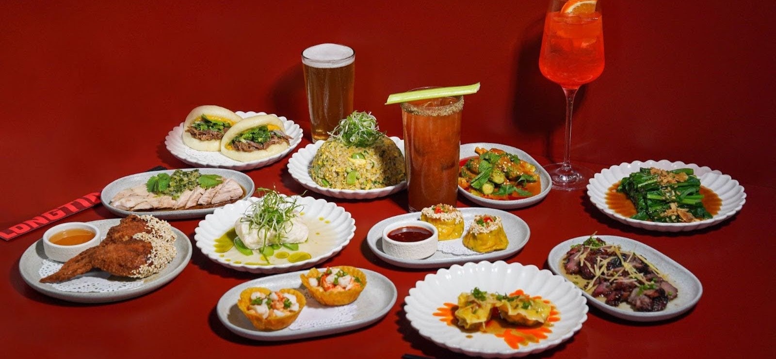 A spread of small plates and drinks on a red table at LONGTIME