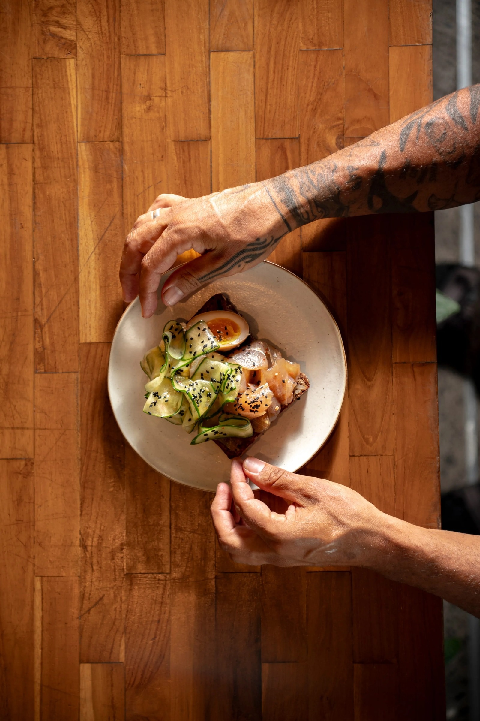 Hands setting down a plated dish on a wooden table at Artisan