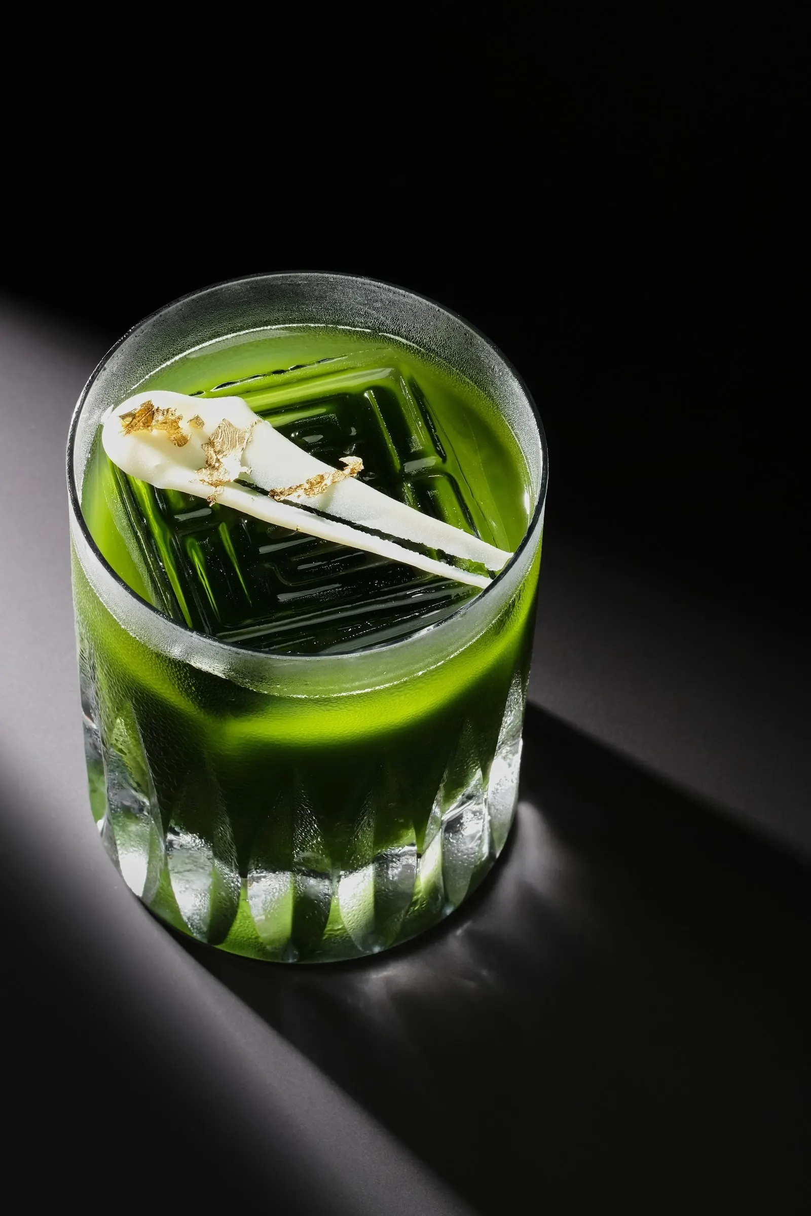 Kind of Blue, a bright green matcha cocktail in a cut-glass tumbler with a leaf garnish.