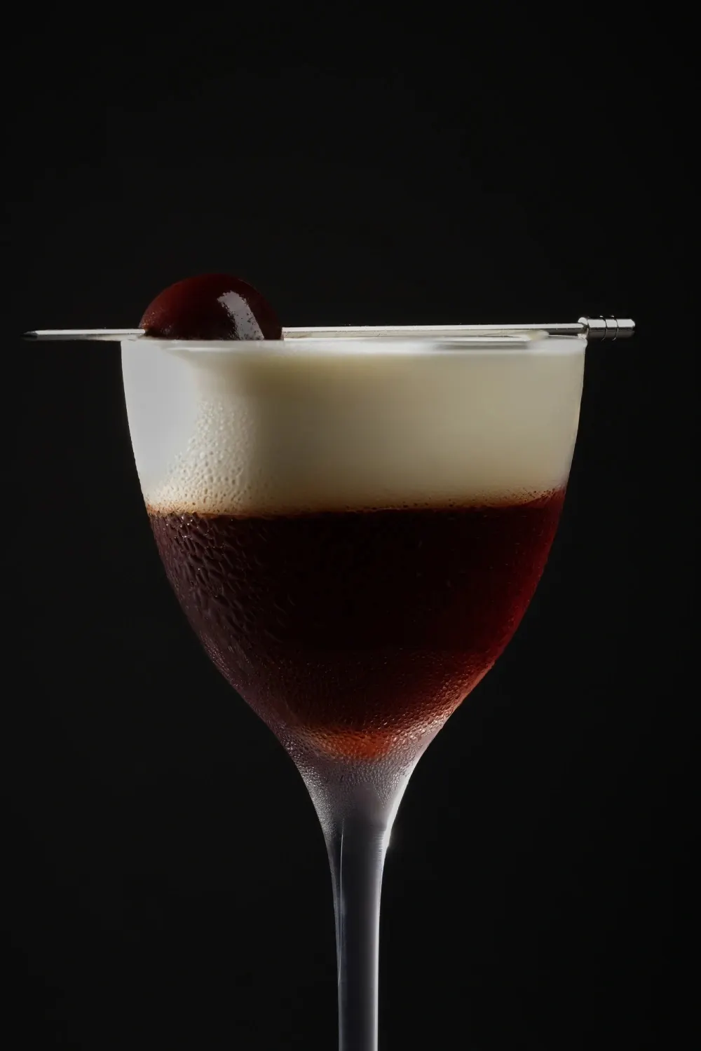 Velvet Cherry, a dark cocktail with a cream top and a cherry pick.