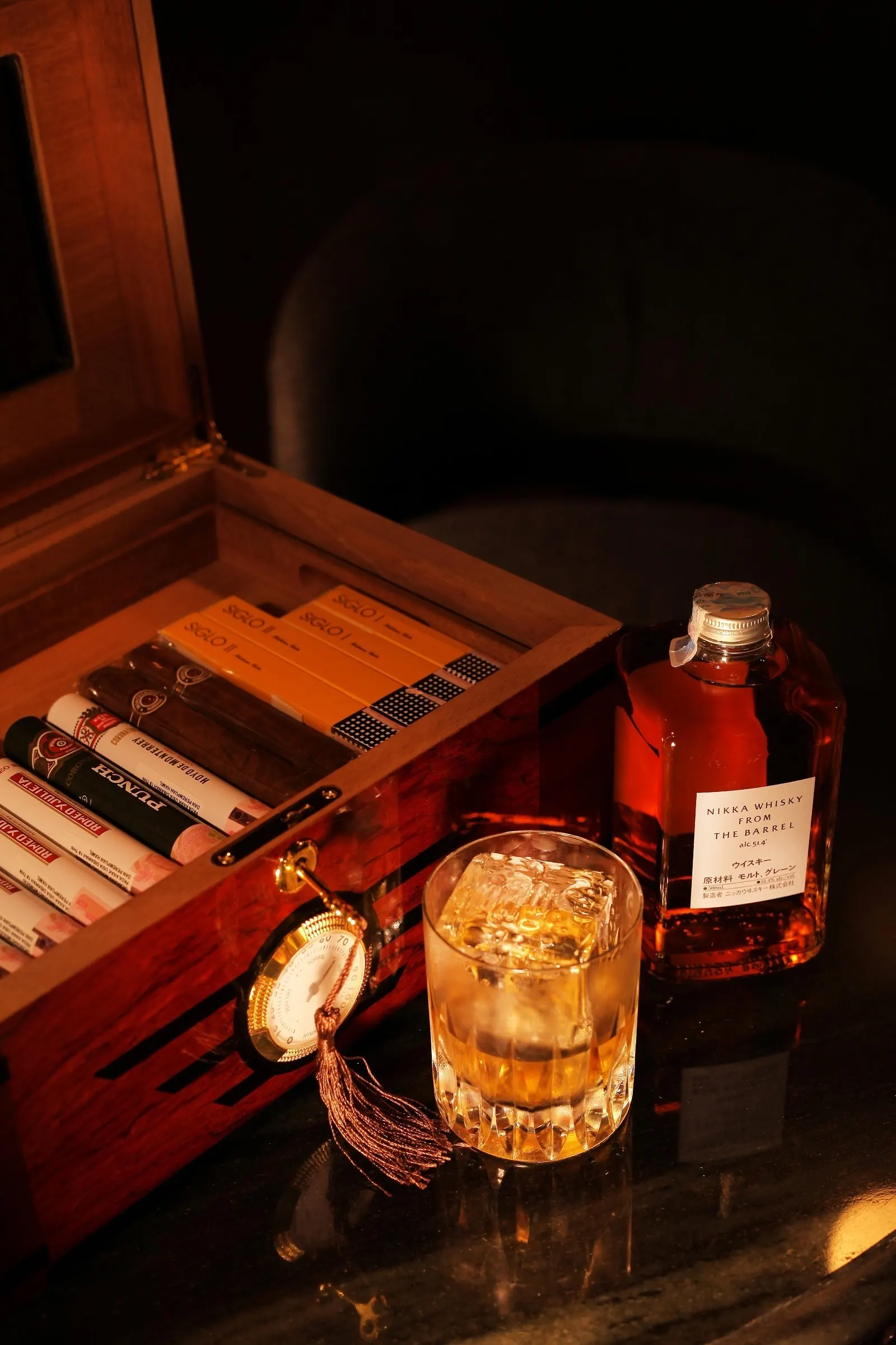 An open humidor of cigars beside a whisky on ice and a bottle at AOKU.